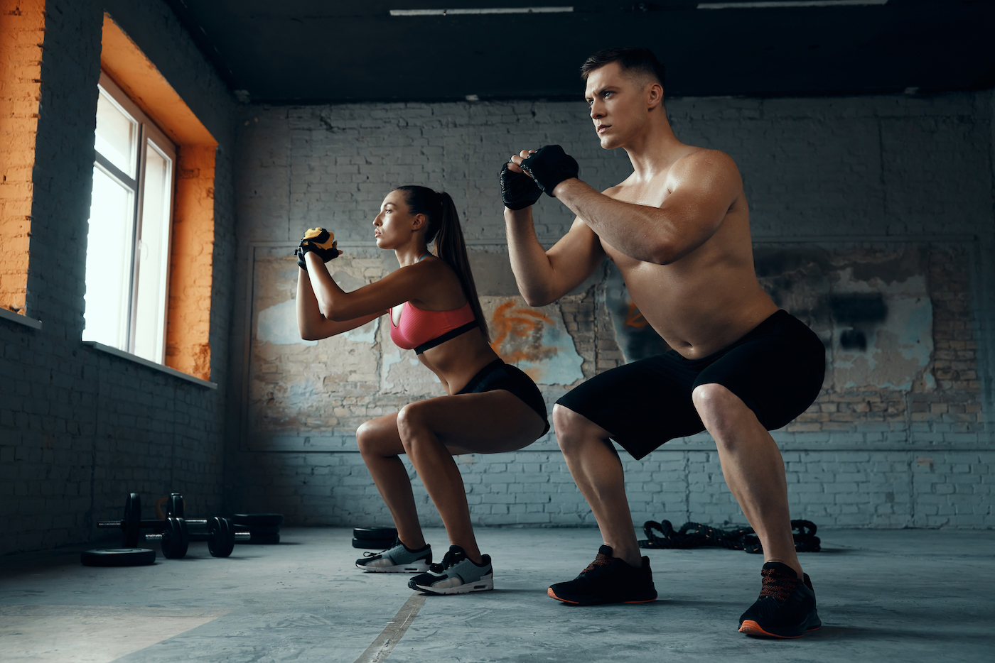 Confident fit couple standing in squatting position while exercising in gym together